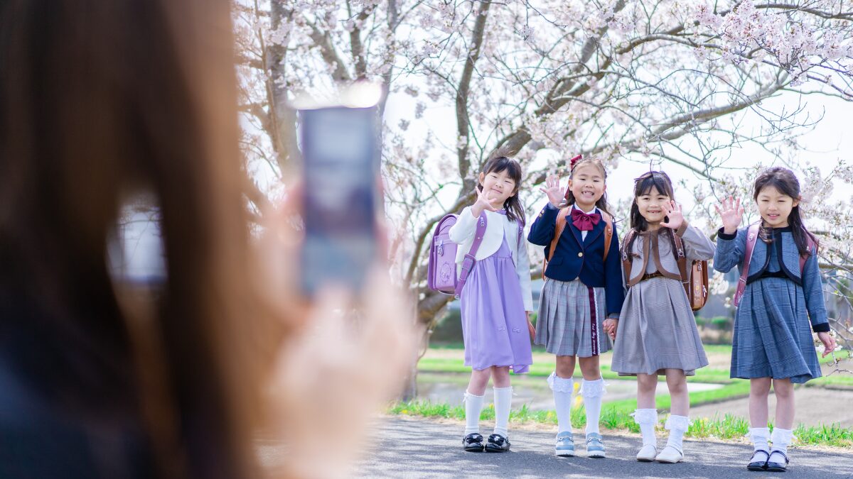 入学式に桜の下で写真を撮る母