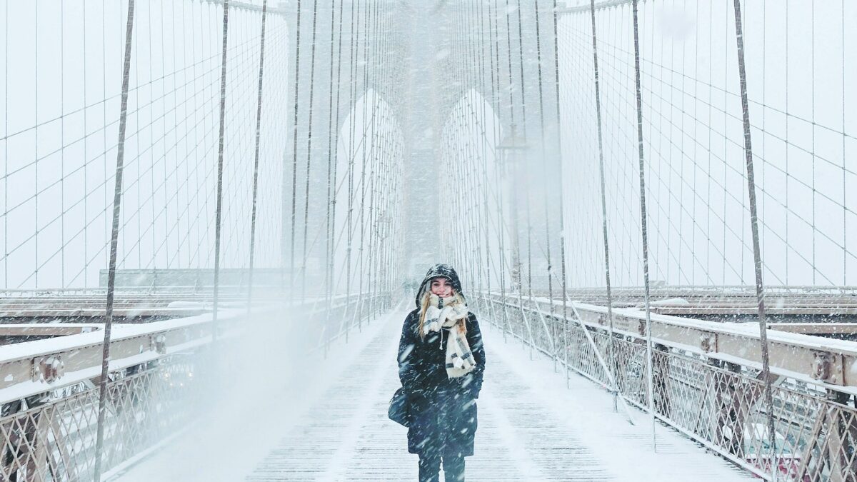 雪が降り積もる橋の上で笑顔を見せるダウンを着た女性