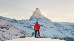 雪山を前に佇む男性。赤生ダウンコートを着ている