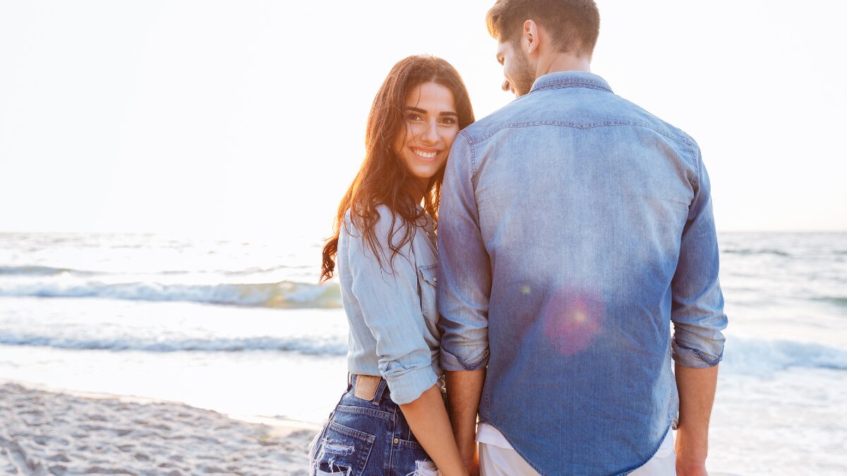 彼氏と手をつなぎながらこちらを振り返る彼女の様子。浜辺のポートレート。