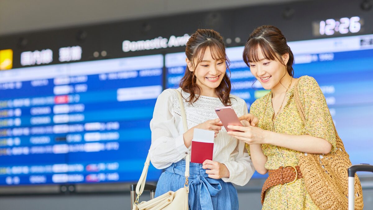 空港でスマホを確認する大学生の女の子2人