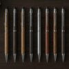 「A top-down flat lay photo of ten luxury mechanical pencils arranged neatly on a dark wooden desk. Includes metal and wood body designs, with a premium leather notebook in the background. Soft natural lighting, realistic photo style, no text or illustrations.」