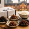 東京駅で買える甘くない佃煮お土産をイメージした、ギフト箱と手土産袋、白ご飯、複数の佃煮小鉢を並べた写真