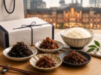 東京駅で買える甘くない佃煮お土産をイメージした、ギフト箱と手土産袋、白ご飯、複数の佃煮小鉢を並べた写真