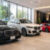 高級車レンタカーの比較をイメージした写真、ショールームに並ぶ複数の高級車、黒い高級セダン、白いSUV、赤いスポーツカー、清潔で高級感のある空間、広告写真風